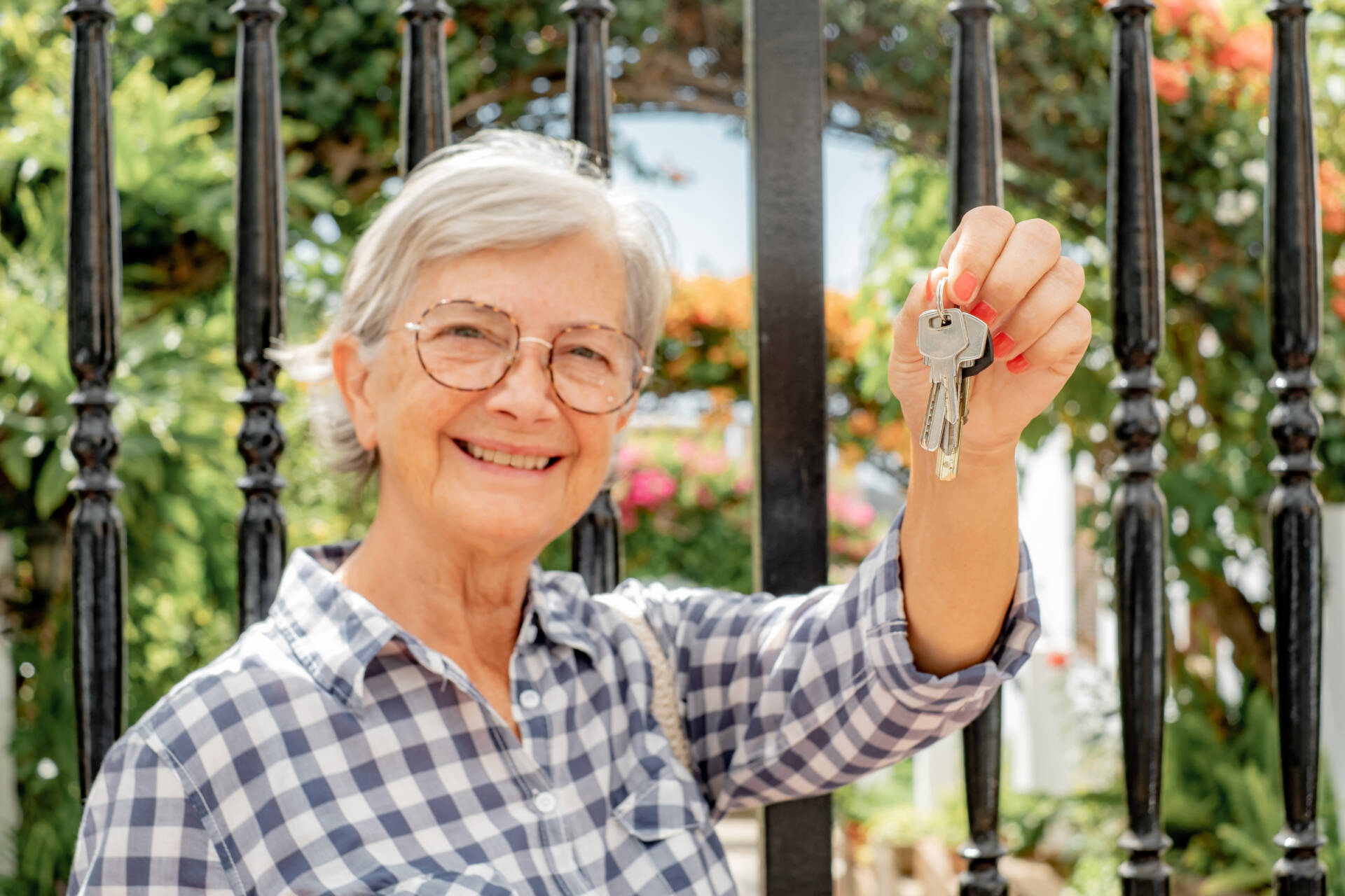 Blurred smiling senior woman at gate holding keys to new home, r